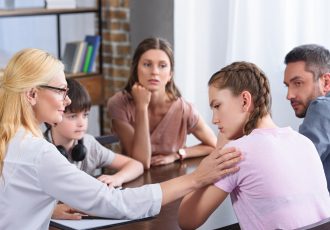 female counselor cheering up upset teenage girl on family therapy session in office